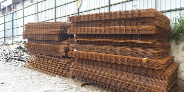 Stacks of rusted steel reinforcement mesh panels stored outdoors.